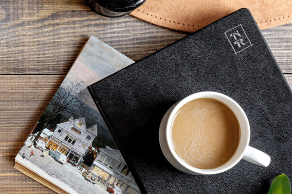 Cup of coffee on a leather-bound notebook with "NR" insignia for celebrity brand vision and website design.