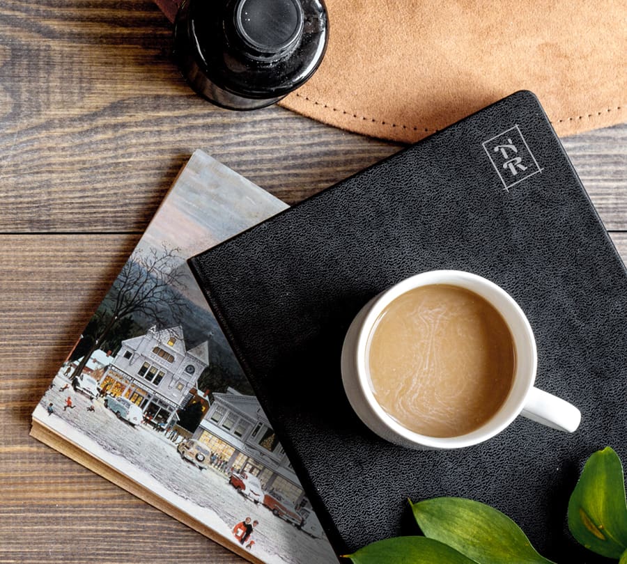 Cup of coffee on a leather-bound notebook with "NR" insignia for celebrity brand vision and website design.